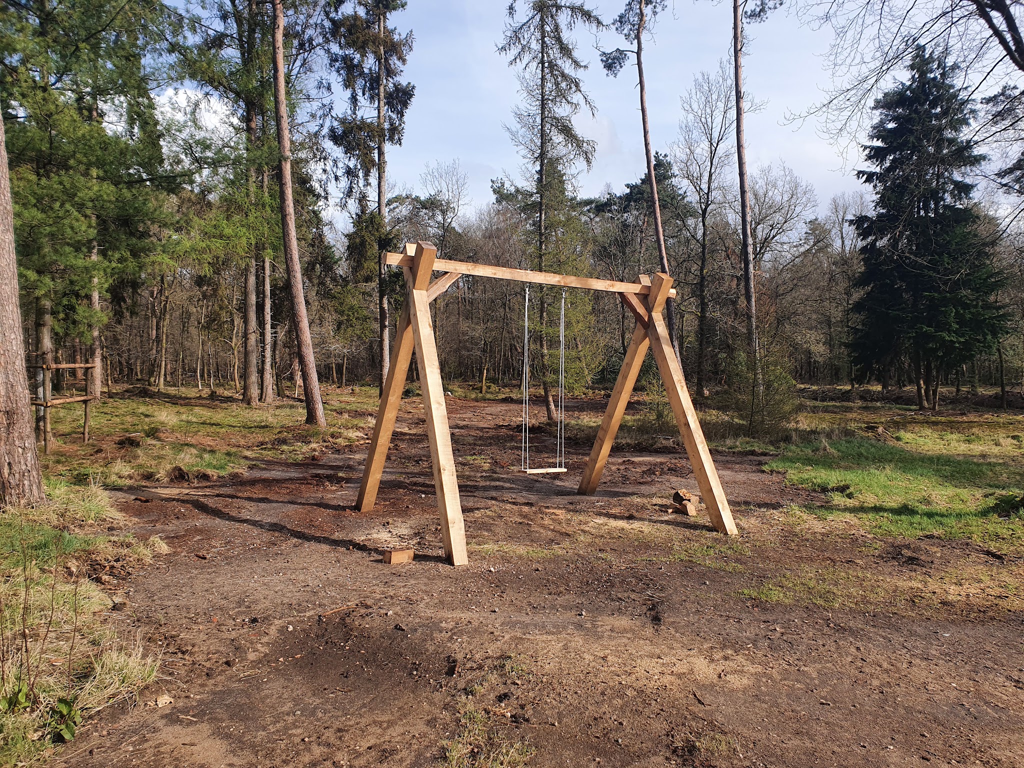 Houten schommel van zware balken op een pas aangelegd stuk grond tussen de bomen