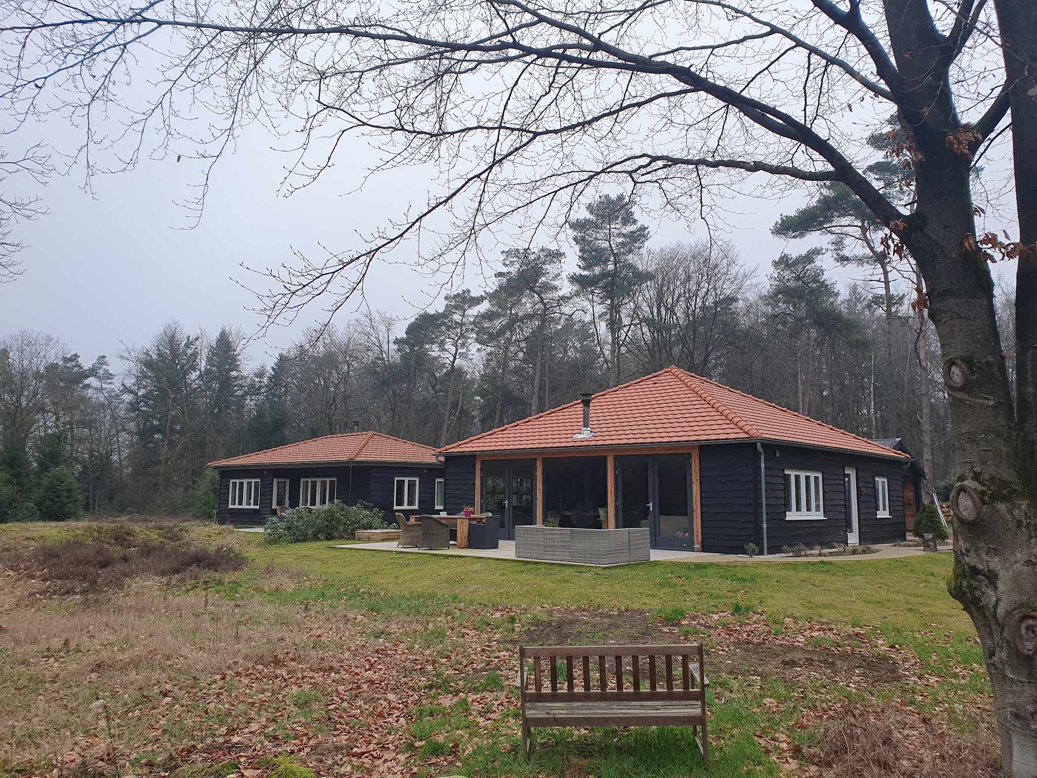 Zwart houten bungalow met oranje pannendak en overdekte veranda, gebouwd door Klusbedrijf Fabricius Kooij